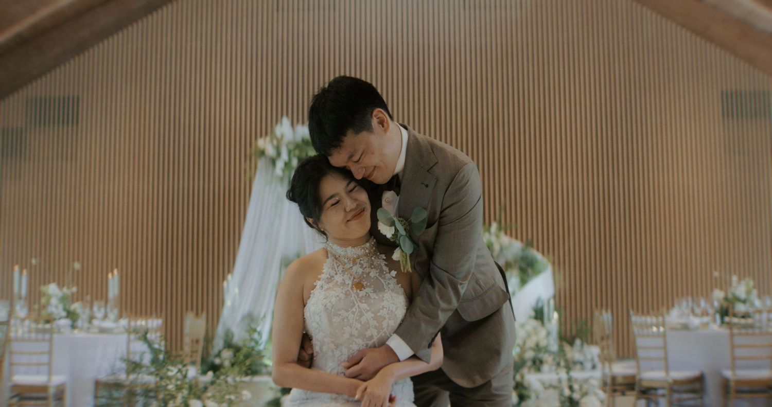 A couple embraces during their wedding ceremony in an elegantly decorated indoor venue with floral arrangements.