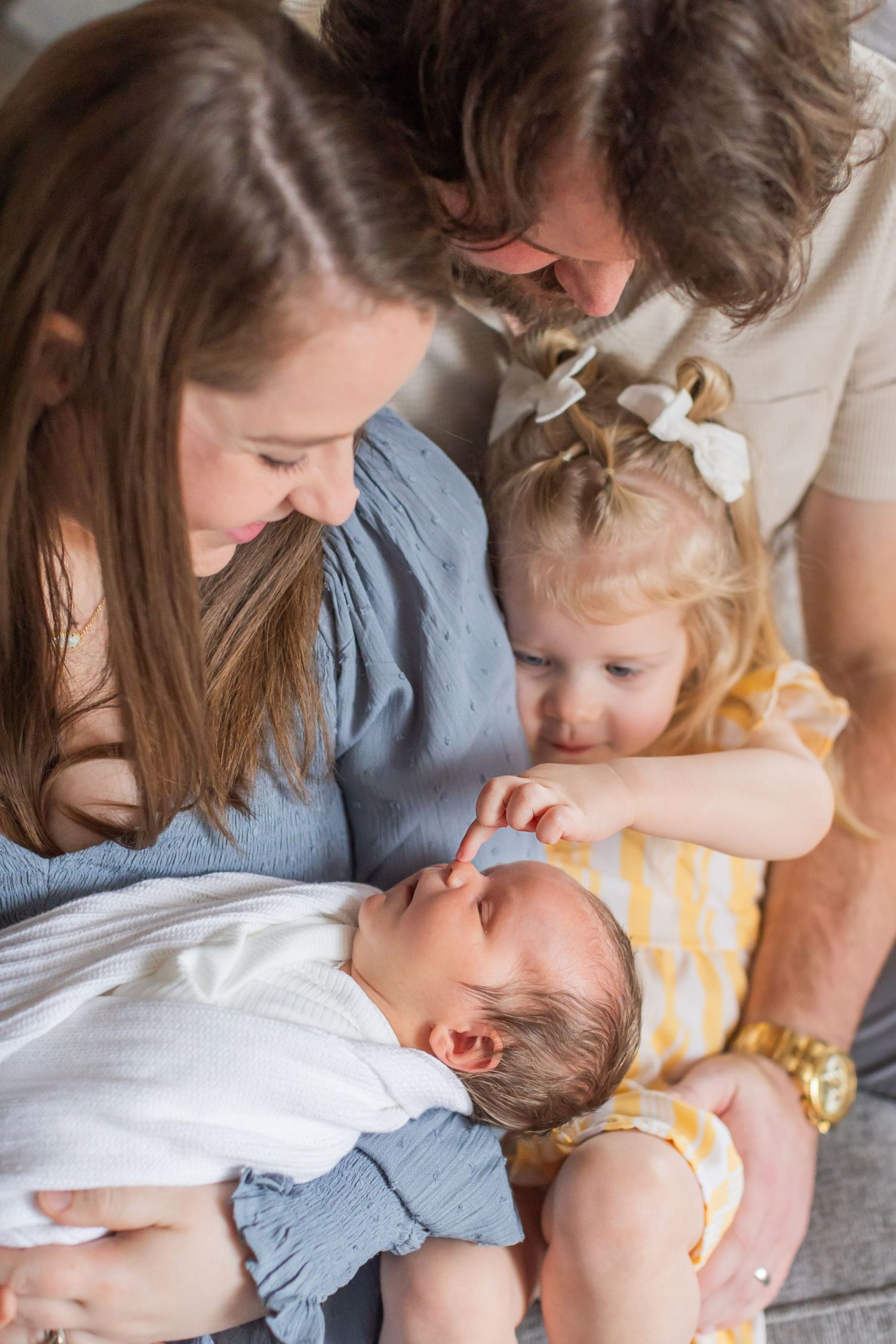 Family sharing tender moment together with newborn baby and toddler on couch in natural light.