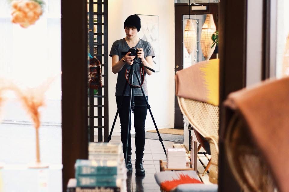 A photographer wearing a black t-shirt and jeans sets up a shot with a tripod in a home studio space.
