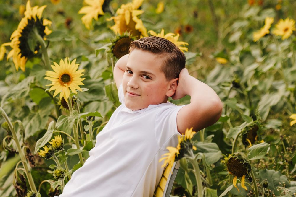 Teen boy poses in a vibrant sunflower field, wearing a white t-shirt, with hand behind head.