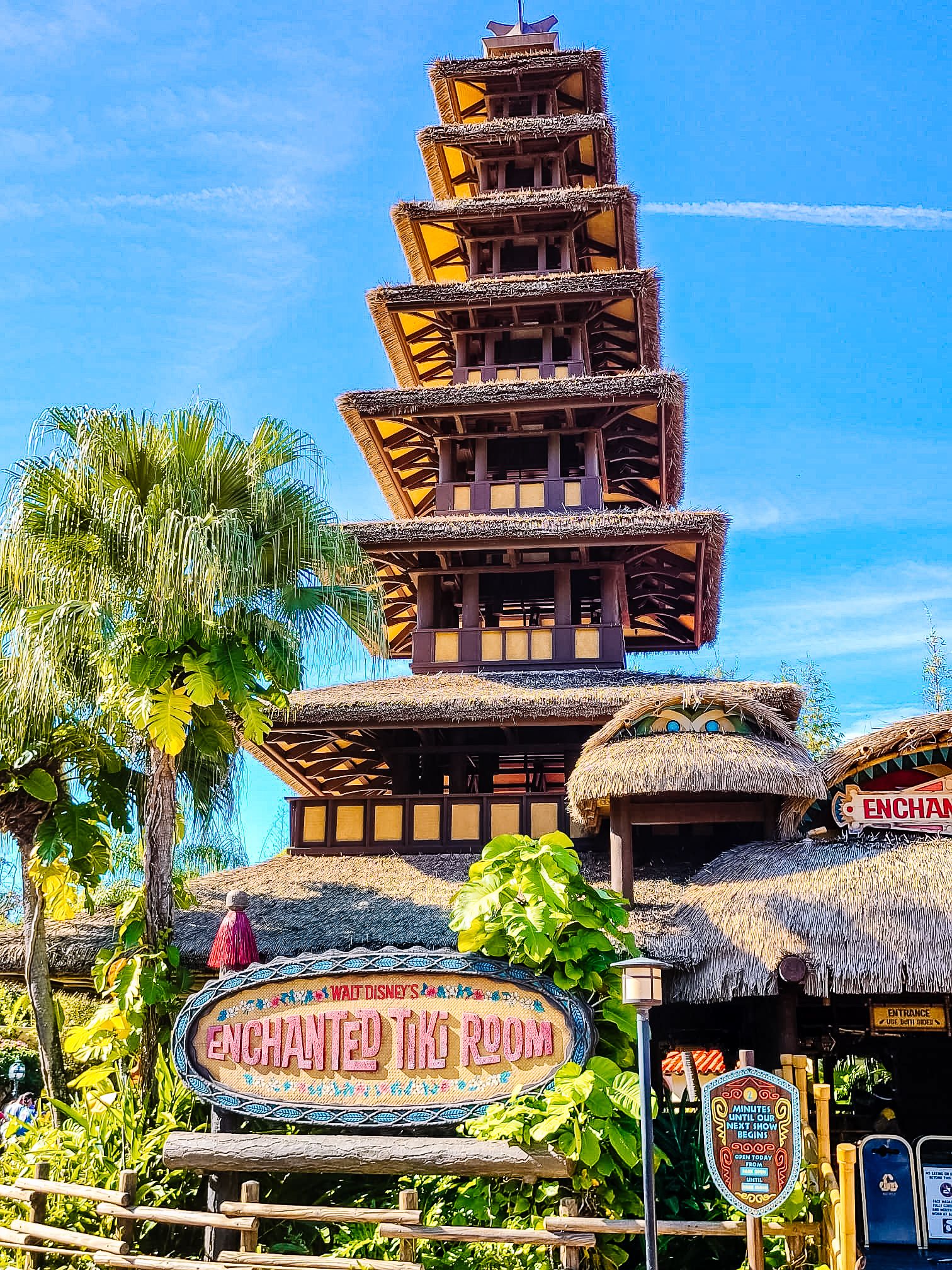 Oriental-style pagoda tower with thatched roof structures at a tropical tiki-themed destination against blue sky.
