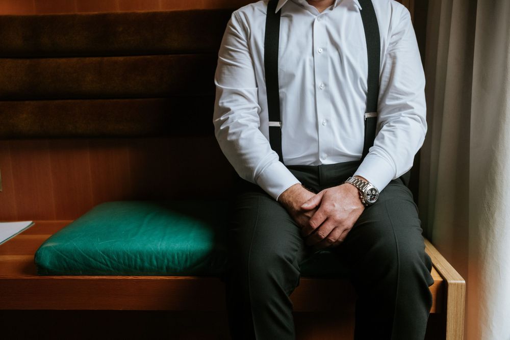 Close-up of person wearing white dress shirt and black suspenders sitting on green bench.