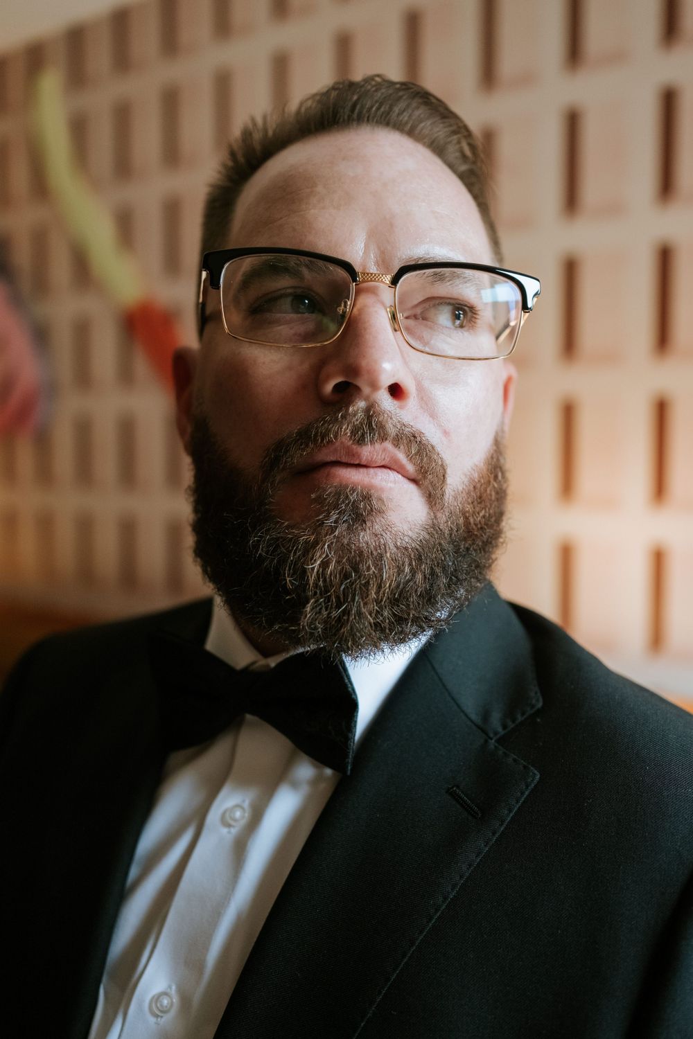 Formal portrait in black suit and glasses against textured wall.