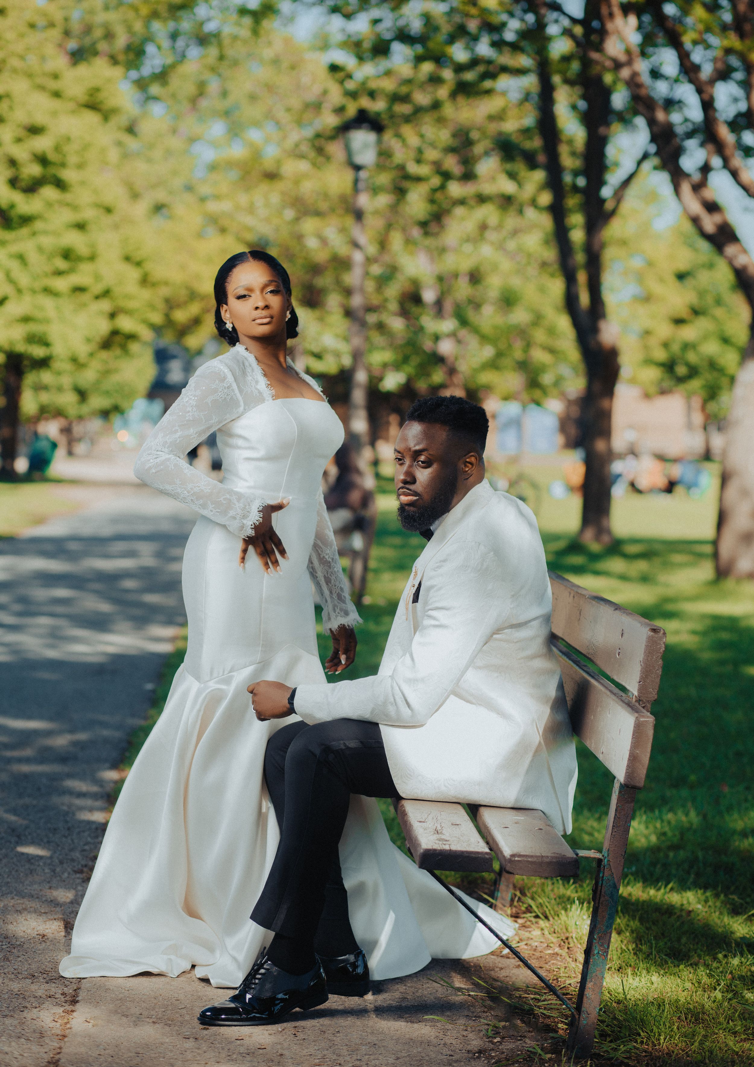 Wedding couple poses on park bench surrounded by trees in stunning formal attire.