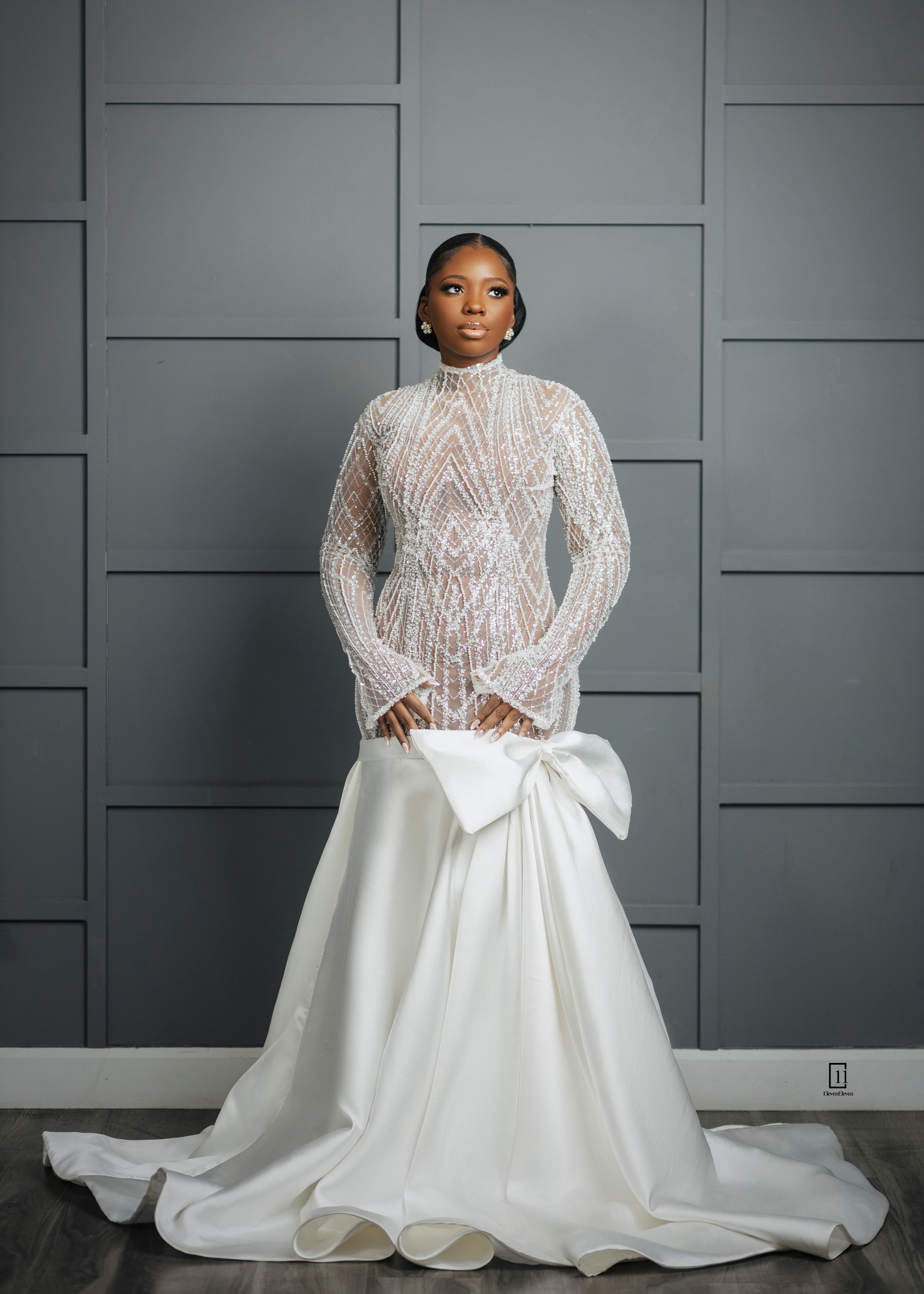 Elegant white wedding gown featuring intricate lace bodice with long sleeves and dramatic bow detail on mermaid silhouette.