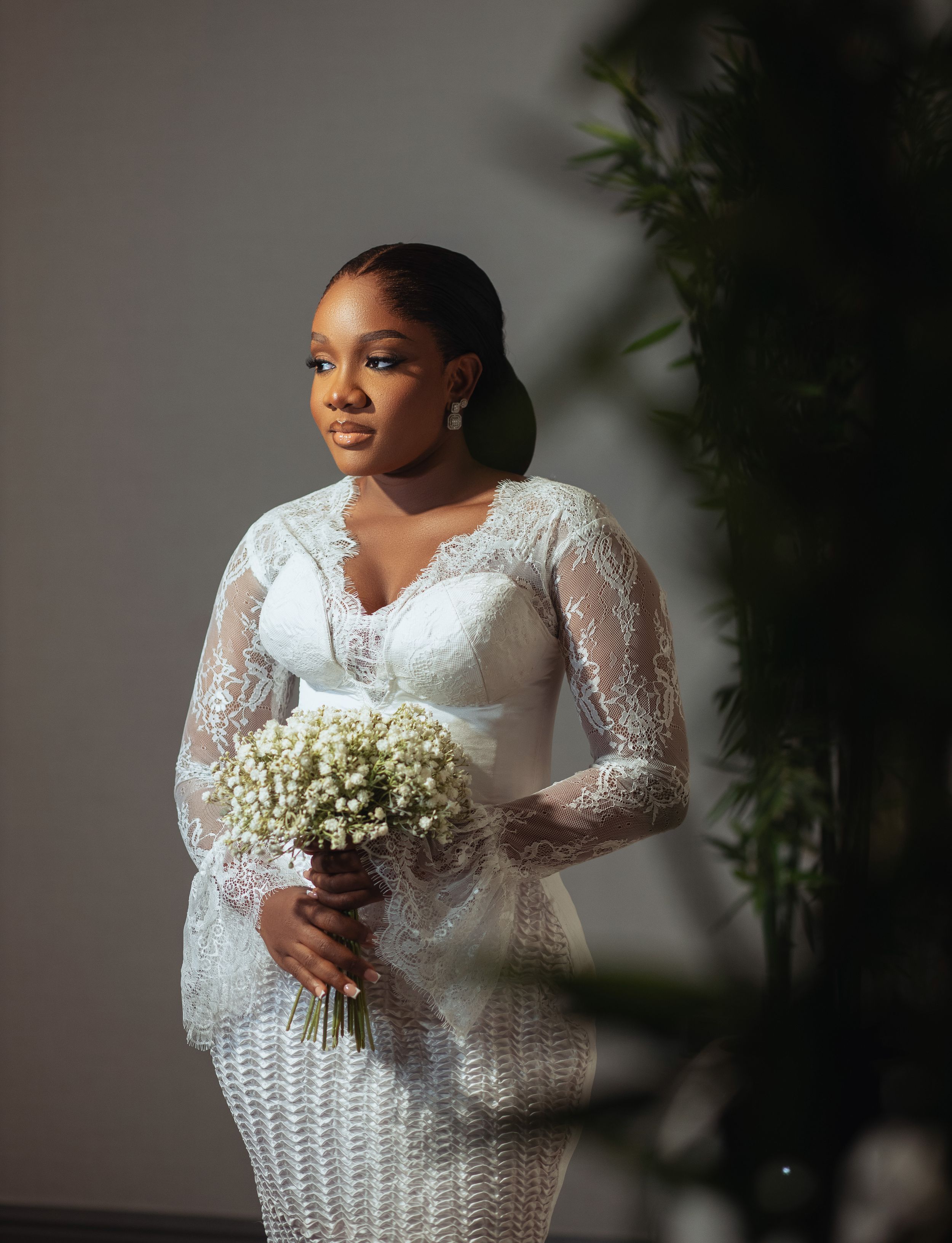 A bride wearing a white lace long-sleeve wedding dress holds a bouquet of baby's breath flowers against a gray backdrop.