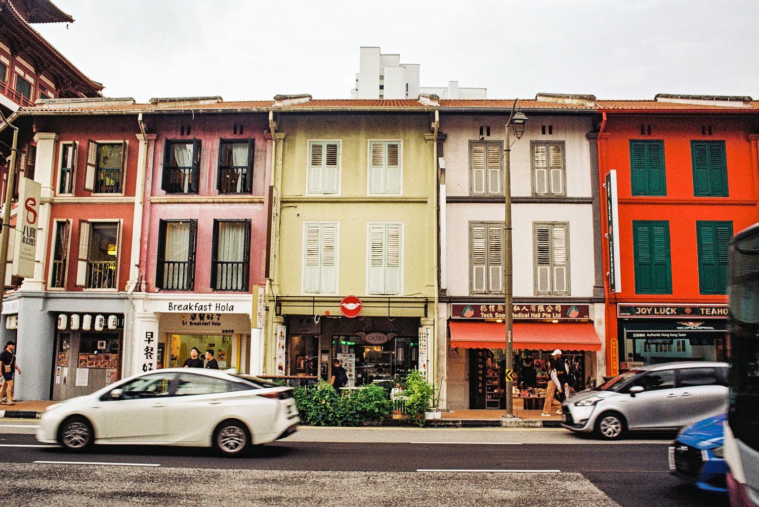 Colorful traditional shophouses line a street in Singapore's historic district with parked cars along the curb. Best time to visit Singapore