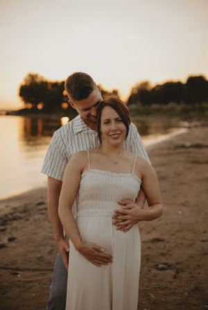 A romantic maternity photo on the beach at sunset with water in the background.