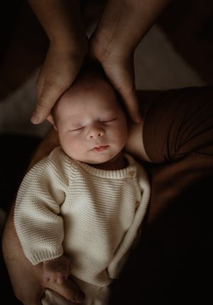 A peaceful sleeping baby in a white sweater with gentle hands touching their head.