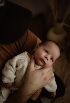 A newborn baby in a cream sweater gazes up while being gently cradled.