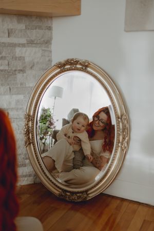 A vintage mirror reflects a sweet moment between parent and child on hardwood floors.