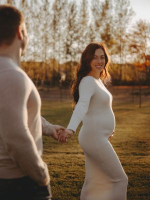 A glowing sunset maternity photo shoot captures an expectant mother in a white dress outdoors.
