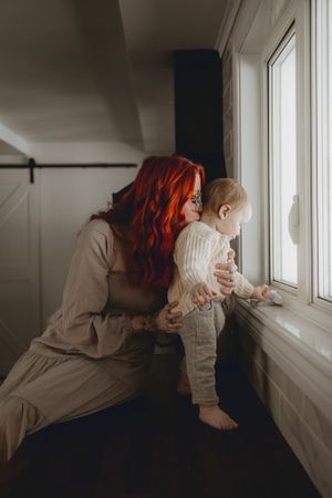 A parent and toddler look out a window together in a tender moment.