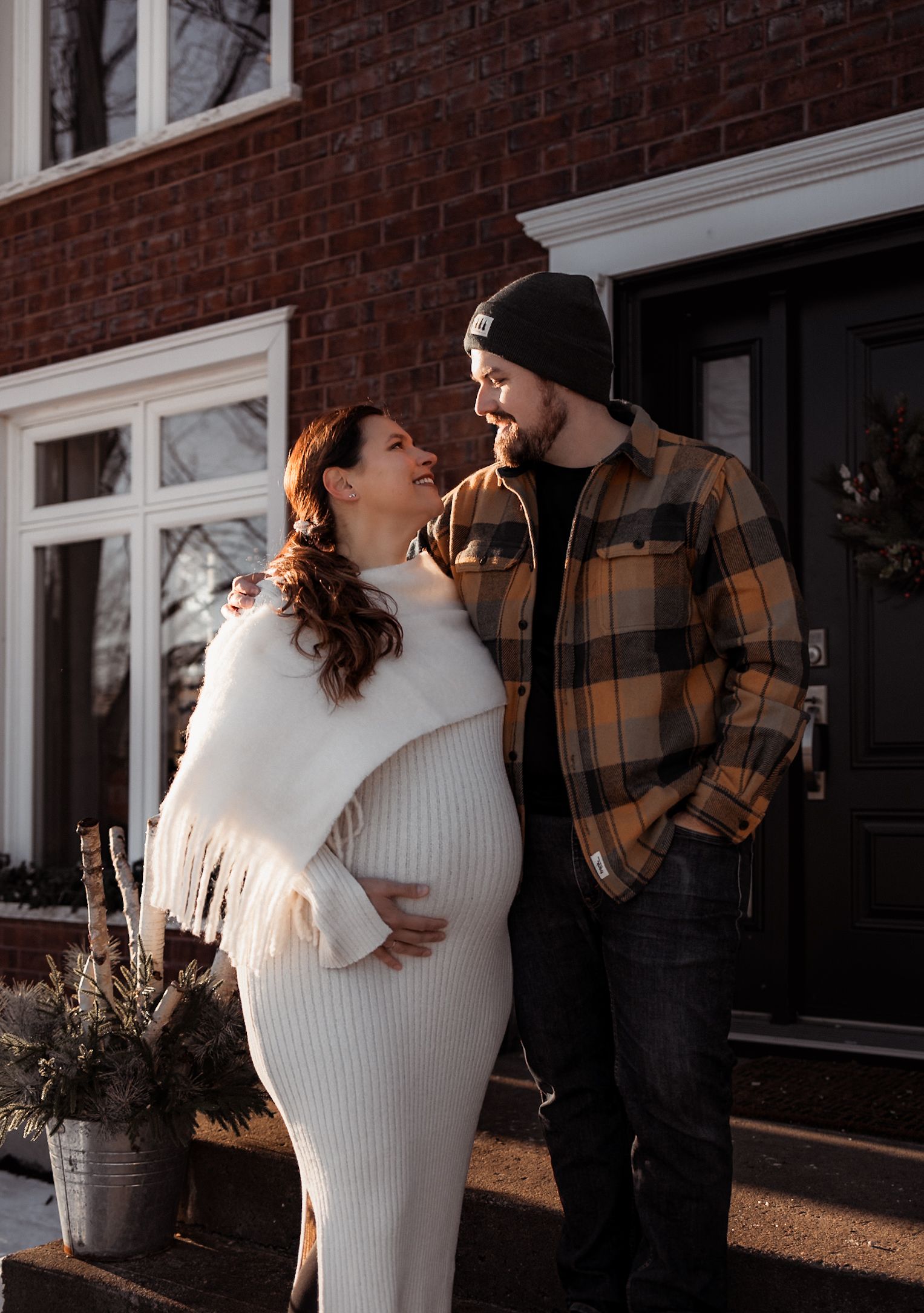 A winter maternity photo outside a brick house with warm clothing.