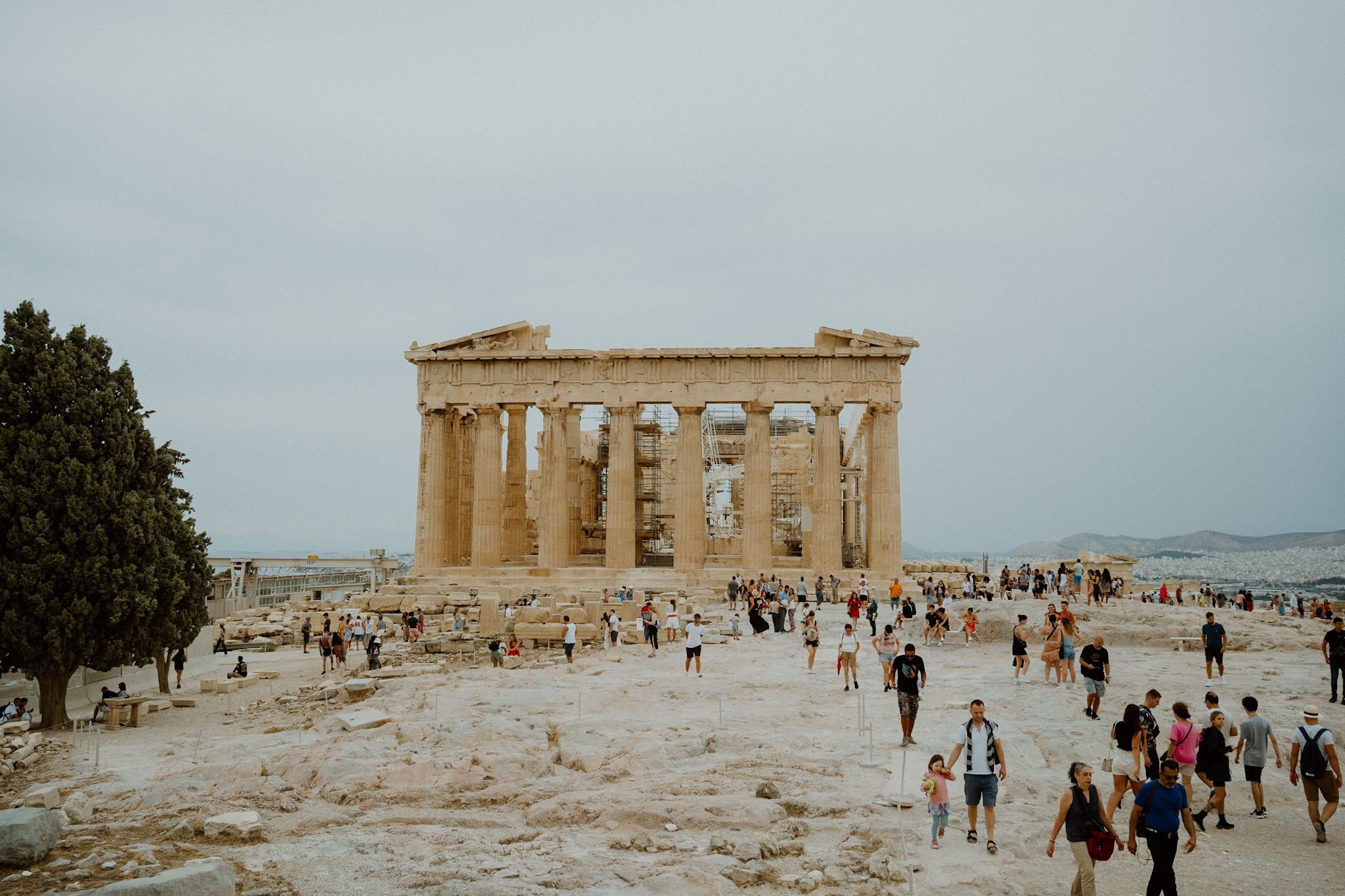 Tourists visit the ancient Parthenon temple on the Acropolis in Athens, Greece under a cloudy sky.