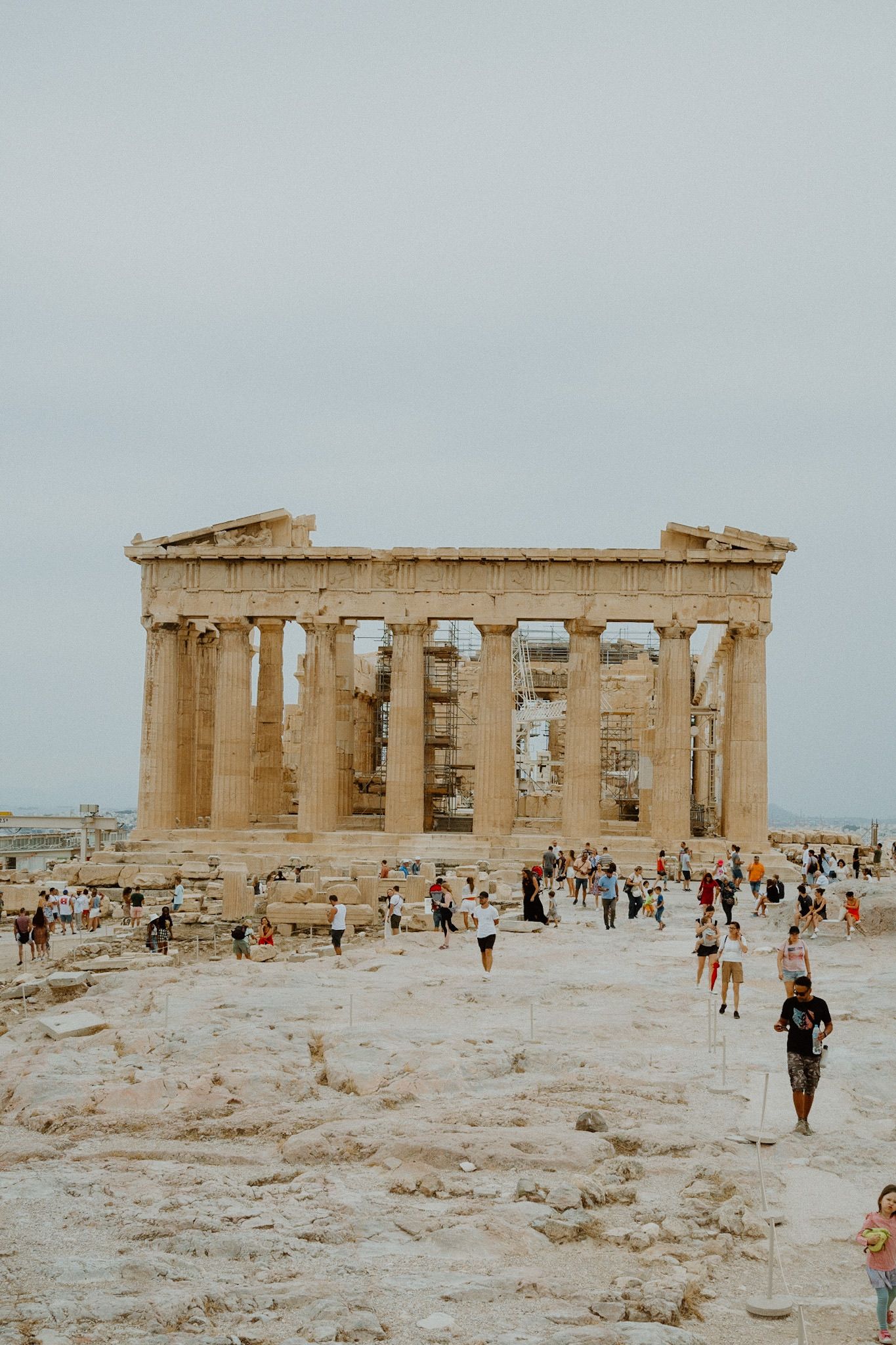 Tourists explore the iconic Parthenon temple on the Acropolis of Athens against a cloudy sky.