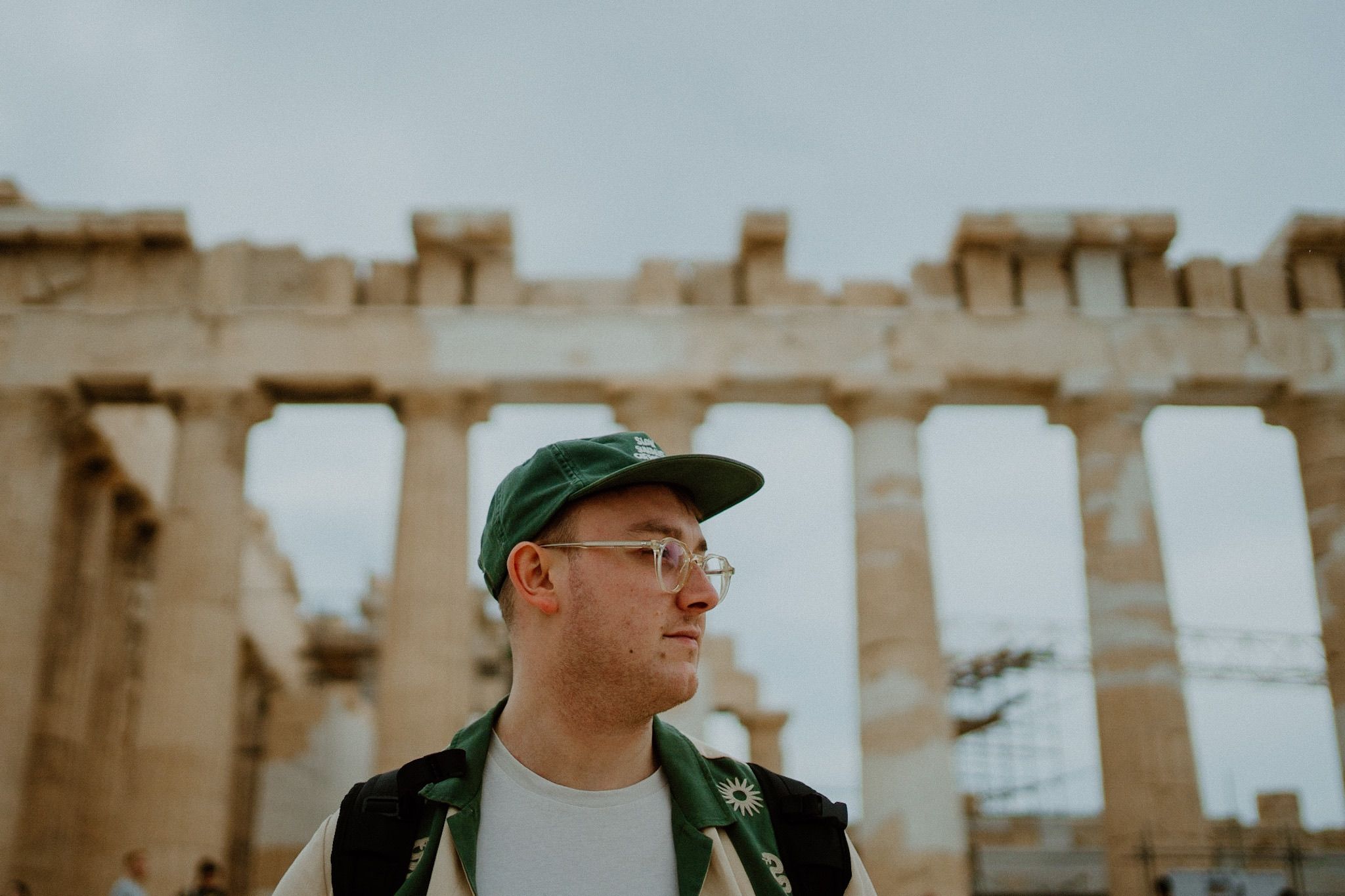 Tourist wearing a green baseball cap and glasses visits the ancient Parthenon ruins in Athens, Greece.