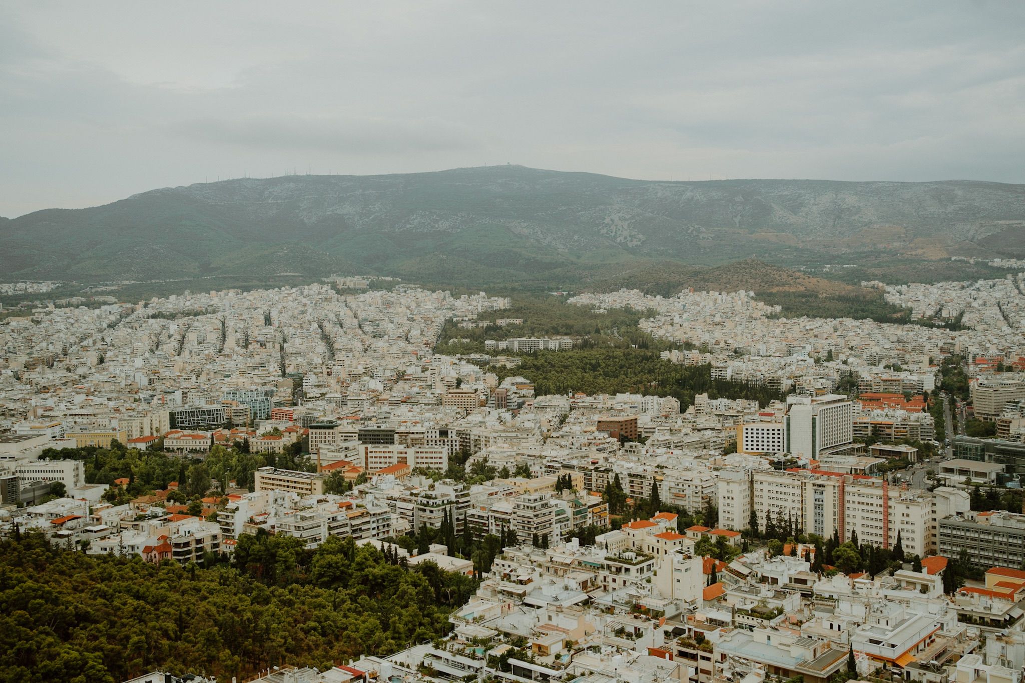 Aerial view of Athens cityscape with densely packed buildings and mountains in the background under cloudy skies.