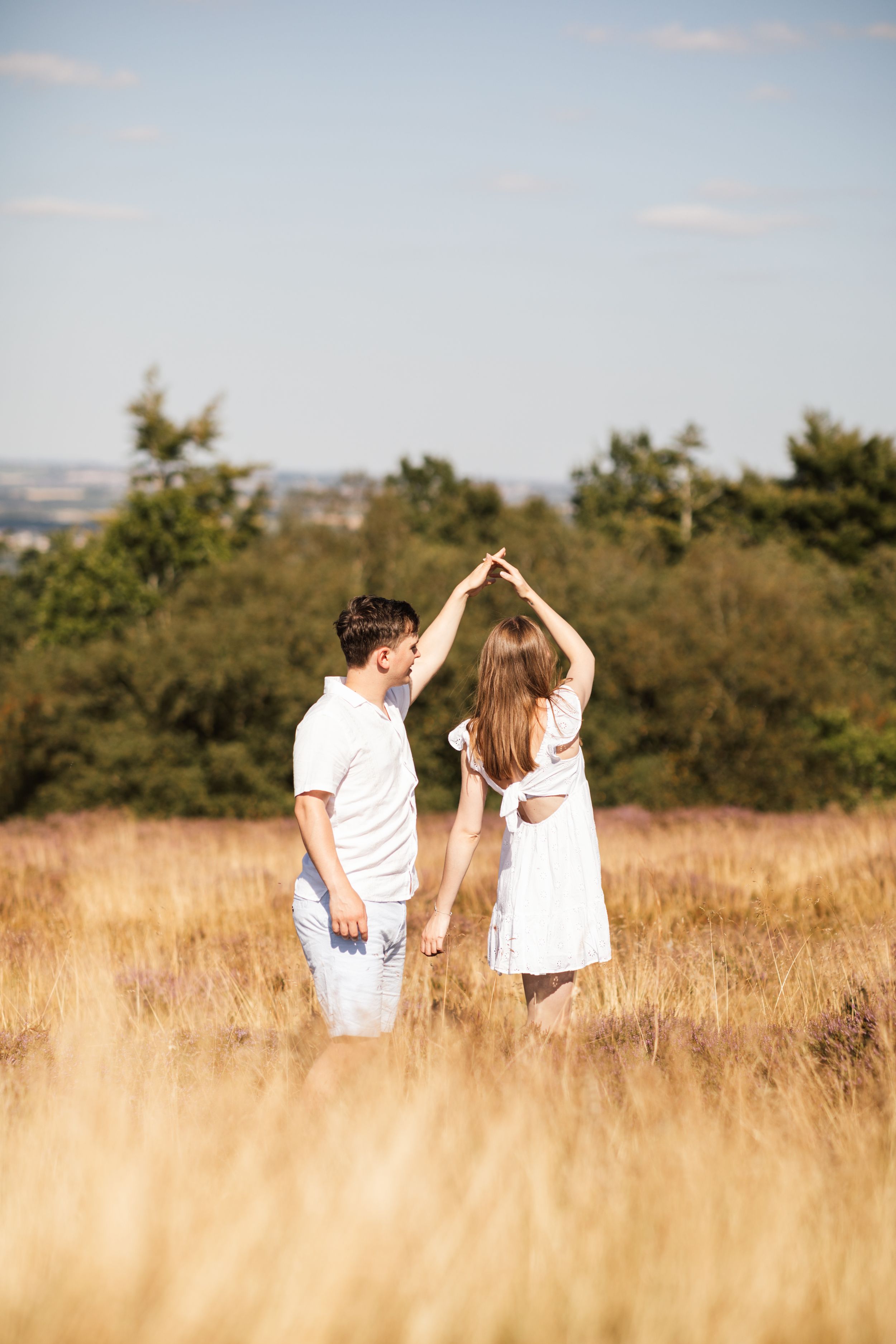 Couple dancing in golden field with summer sky backdrop.