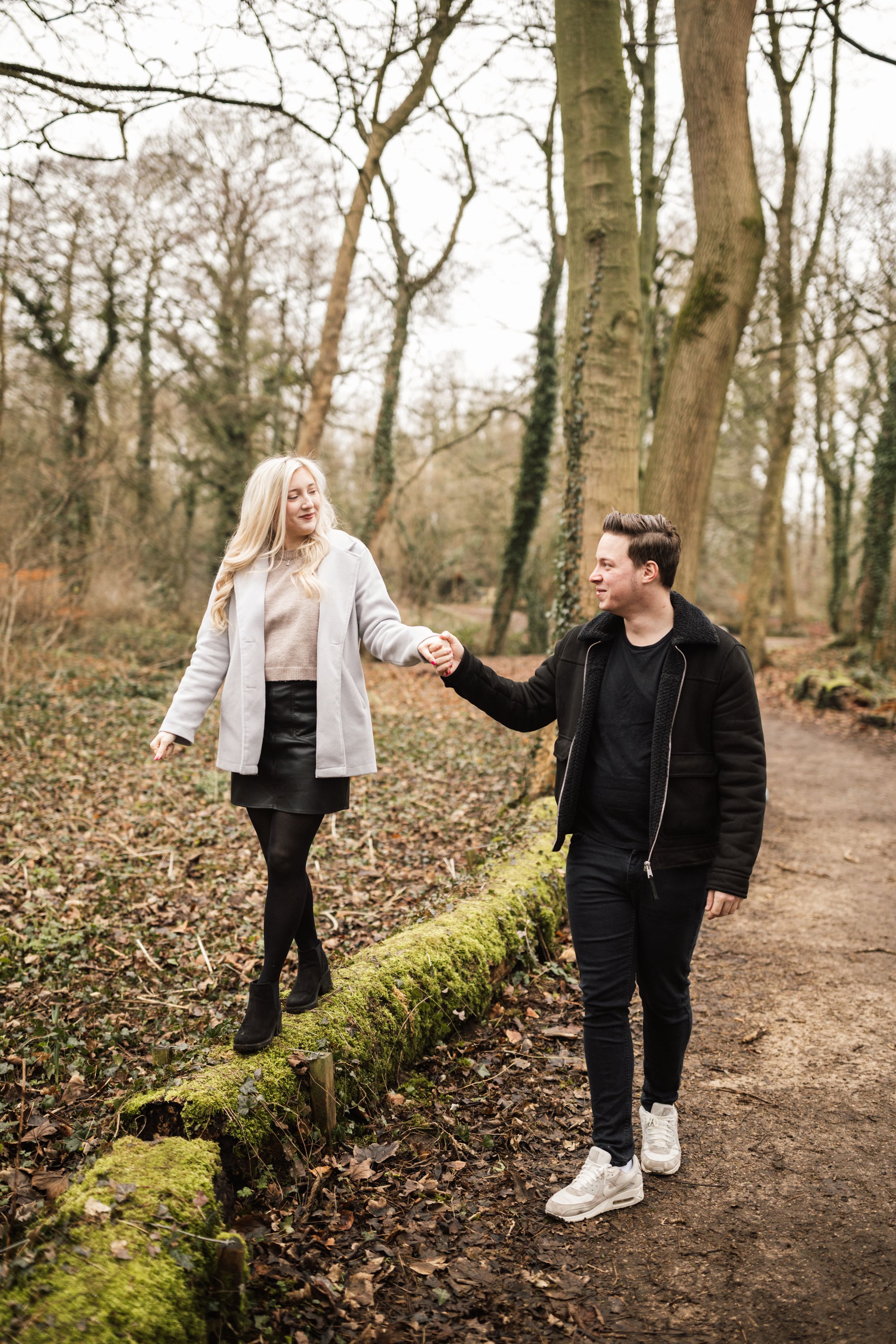 A couple takes a romantic stroll along a moss-covered path in a winter forest.