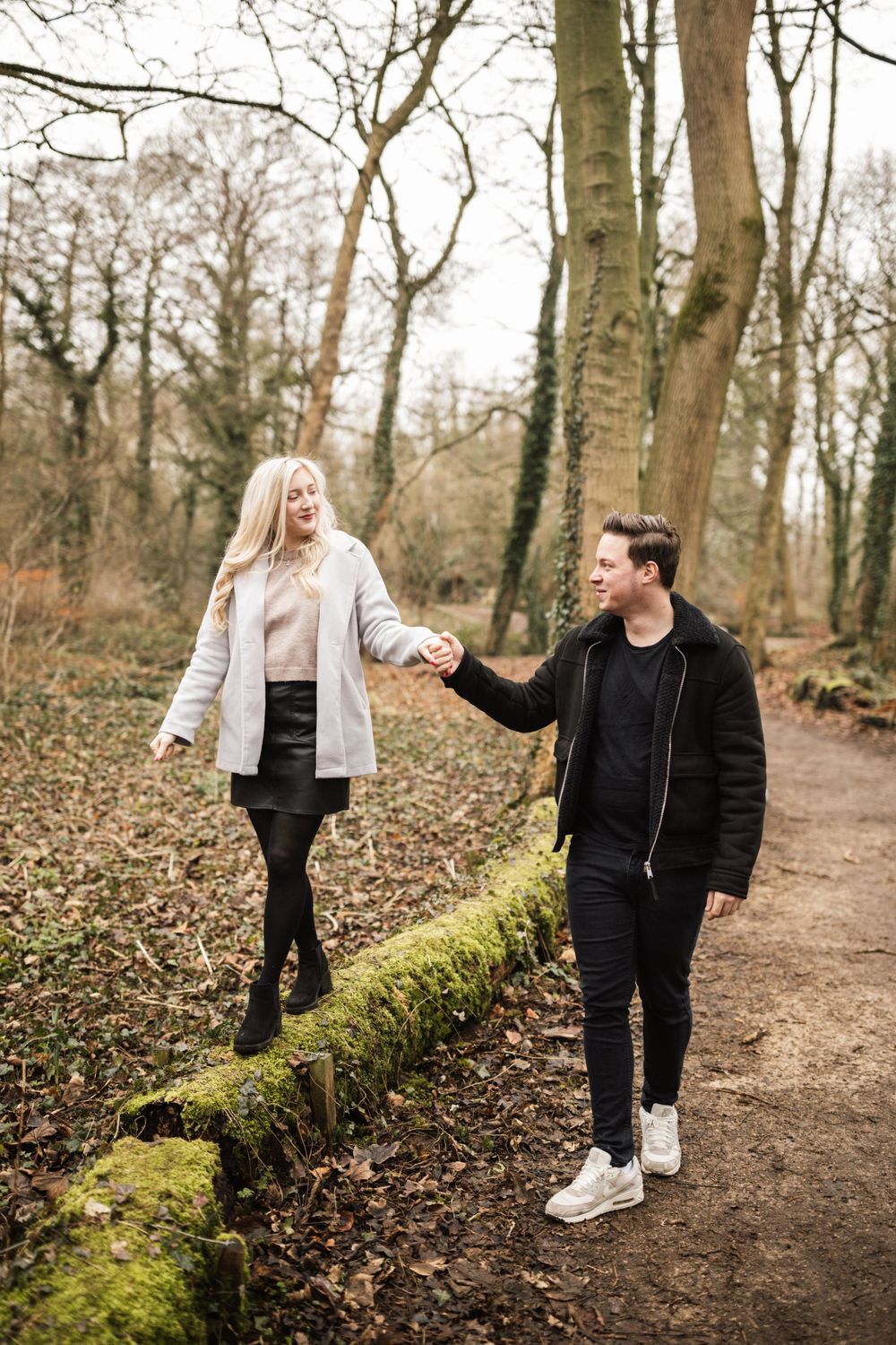 A couple takes a romantic stroll along a moss-covered path in a winter forest.