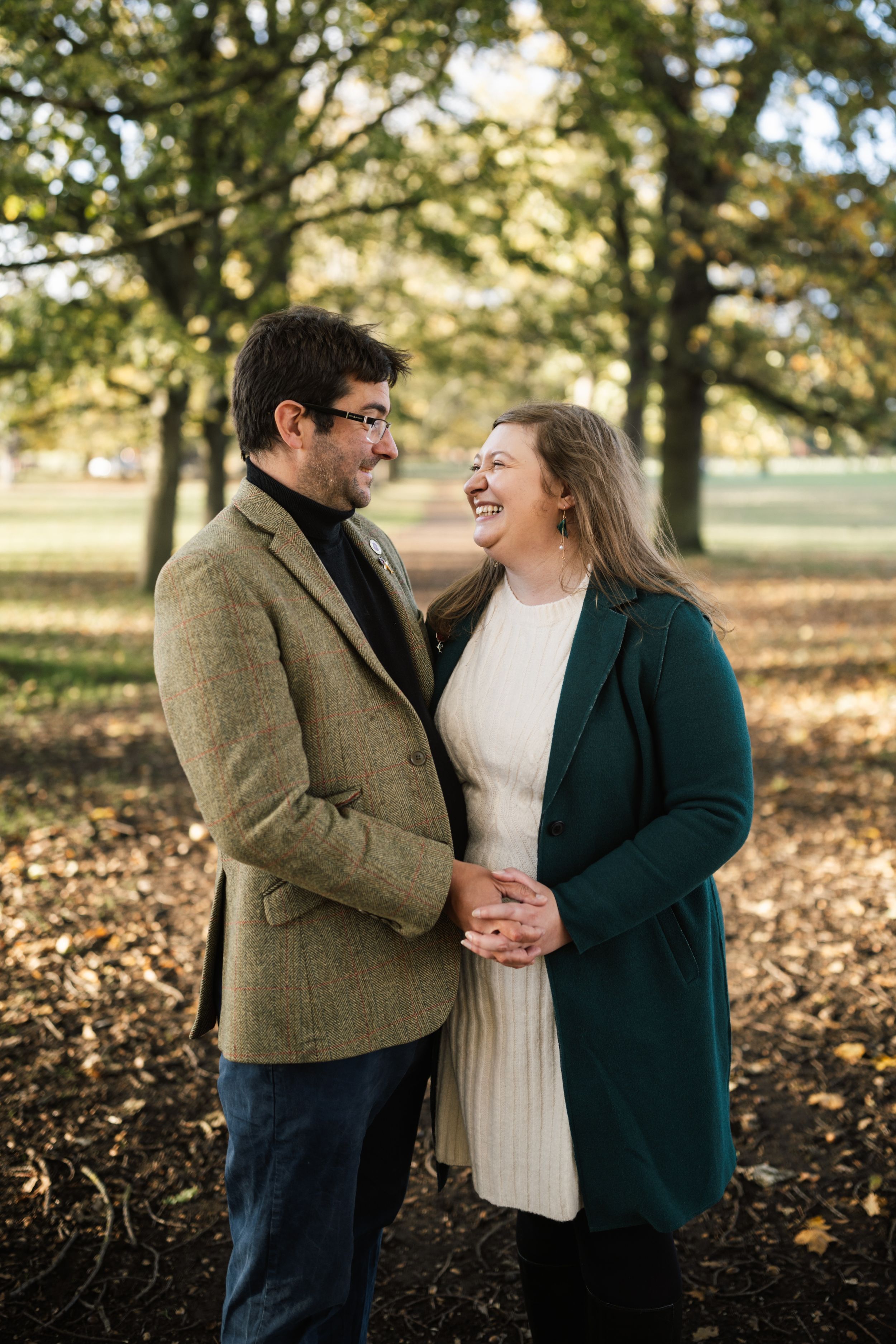 A couple shares joyful moments together on an autumn day with fallen leaves in a park setting.