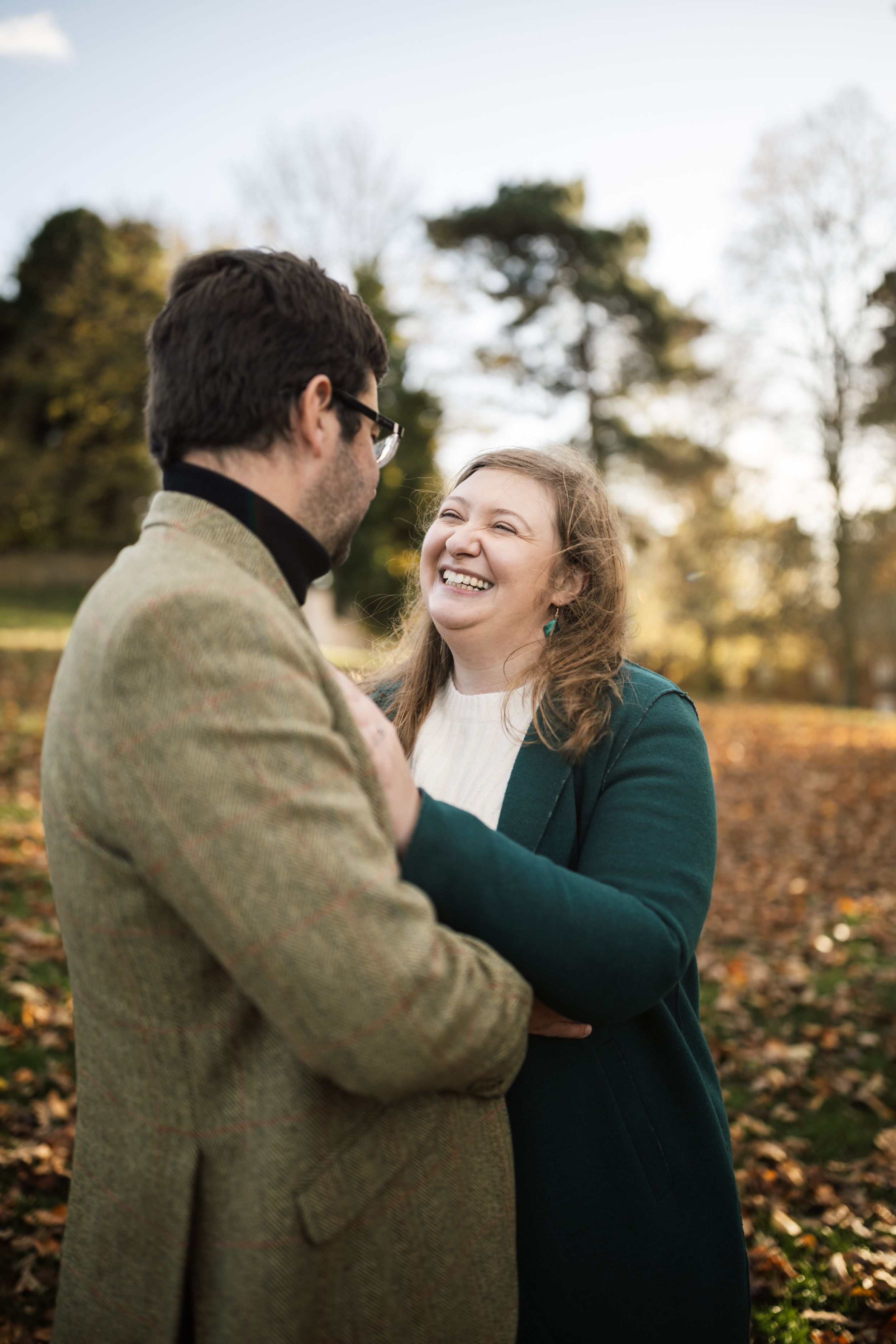 A couple shares a joyful moment together while standing in fallen autumn leaves on a sunny afternoon.