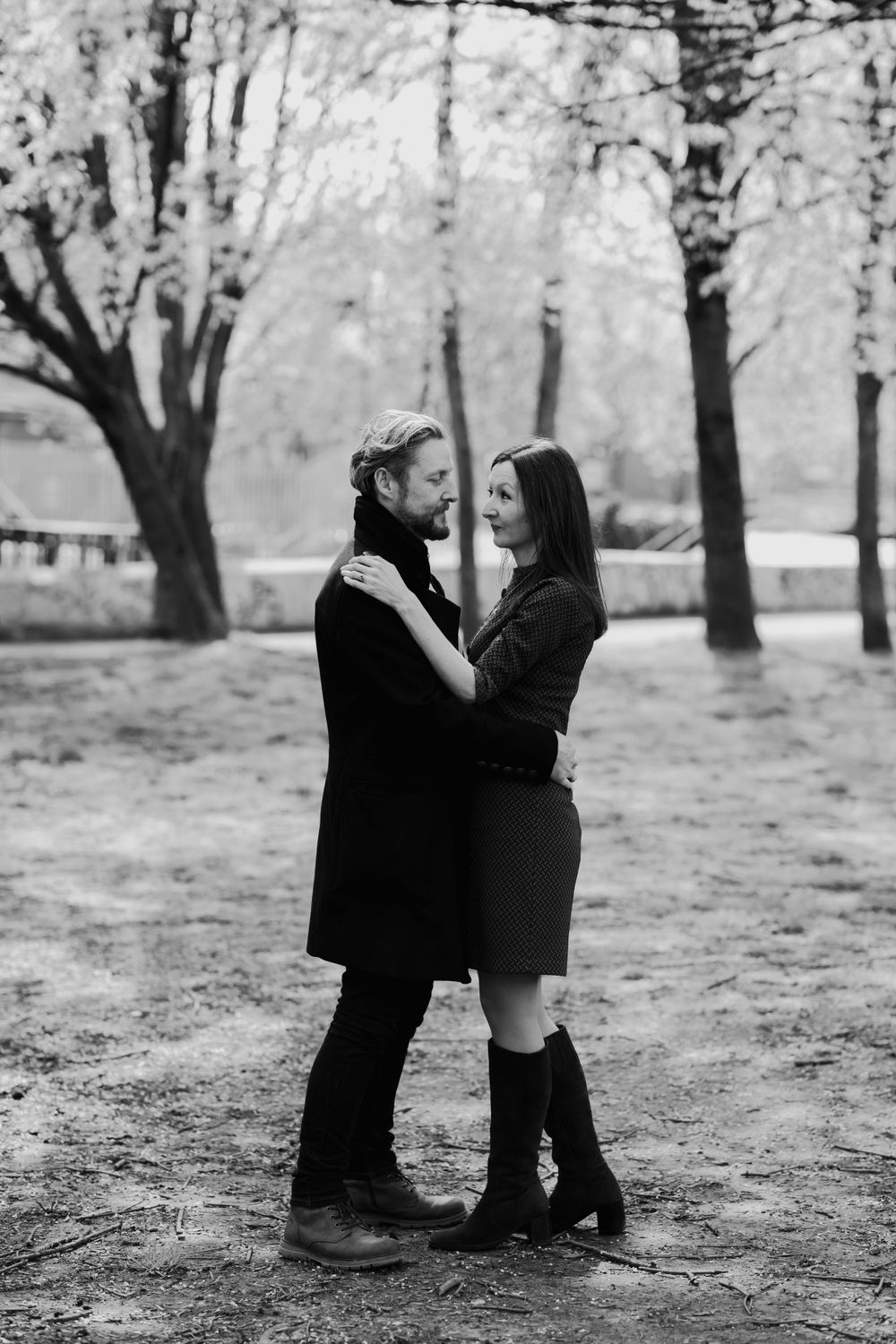 Black and white portrait of couple embracing in a park with bare trees.