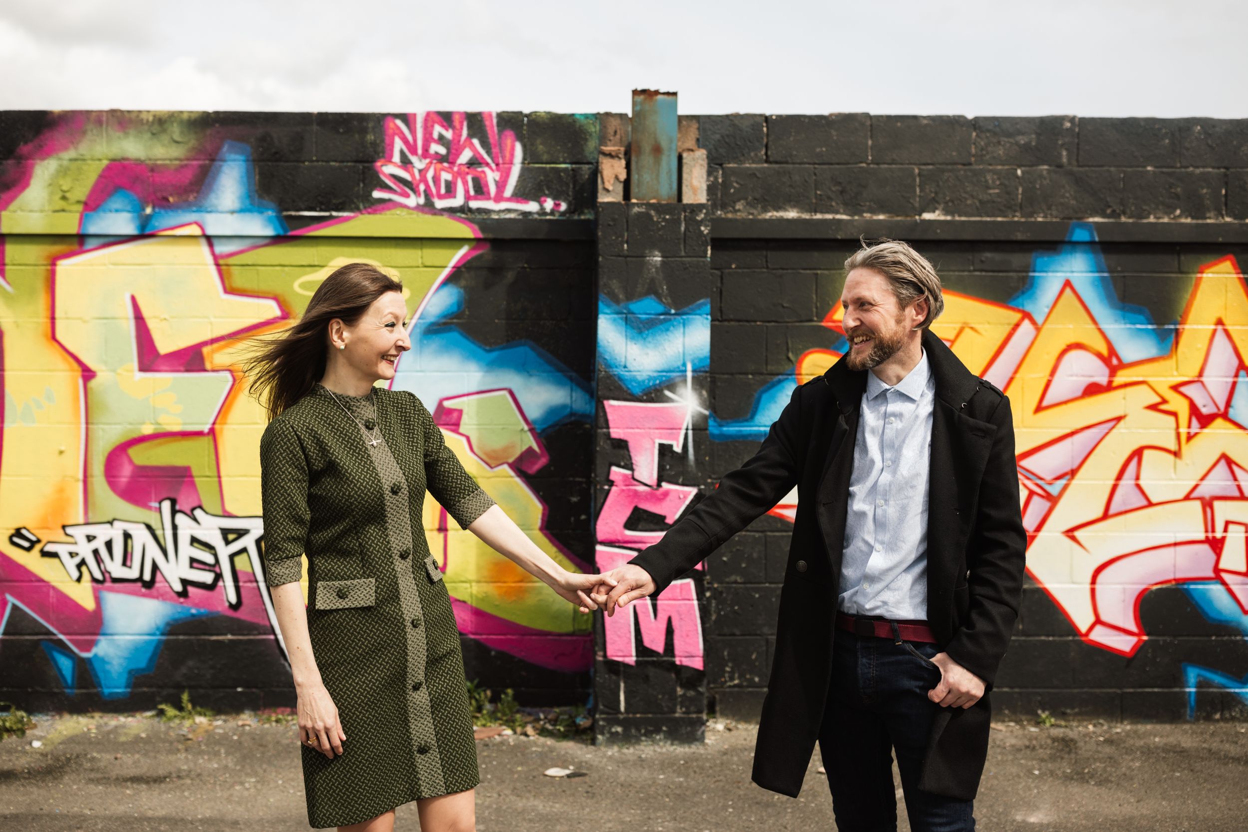 A stylish couple poses playfully in front of vibrant street art murals.