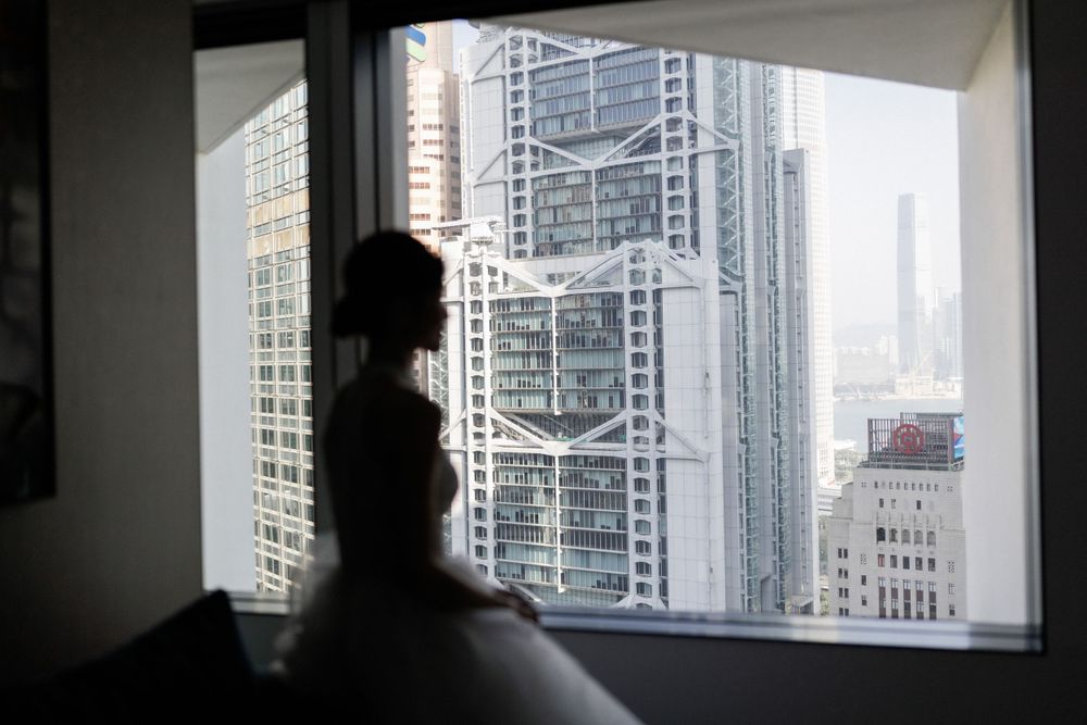 Bride in wedding dress silhouetted against window overlooking urban city skyline.