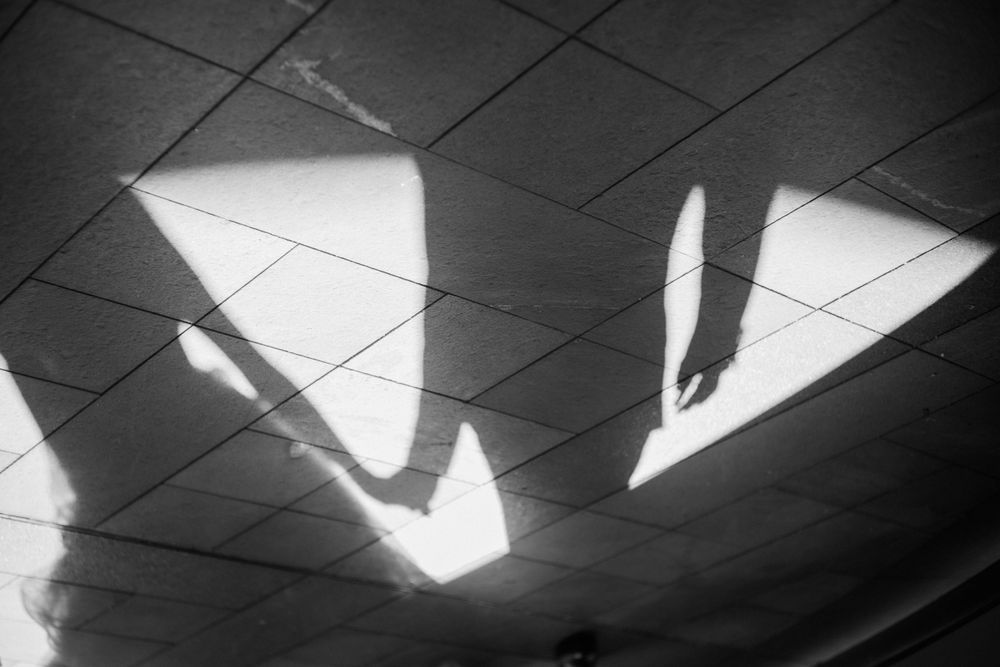 Artistic black and white shadow silhouette of bride and groom on tiled floor.