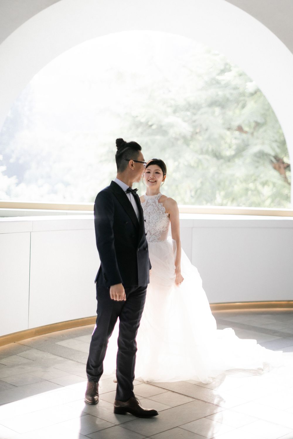 Groom in black tuxedo and bride in white lace gown share first look moment.