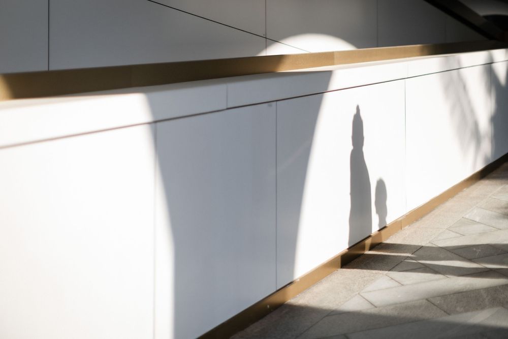 Artistic shadow of bride in wedding gown cast on white wall in sunlight.