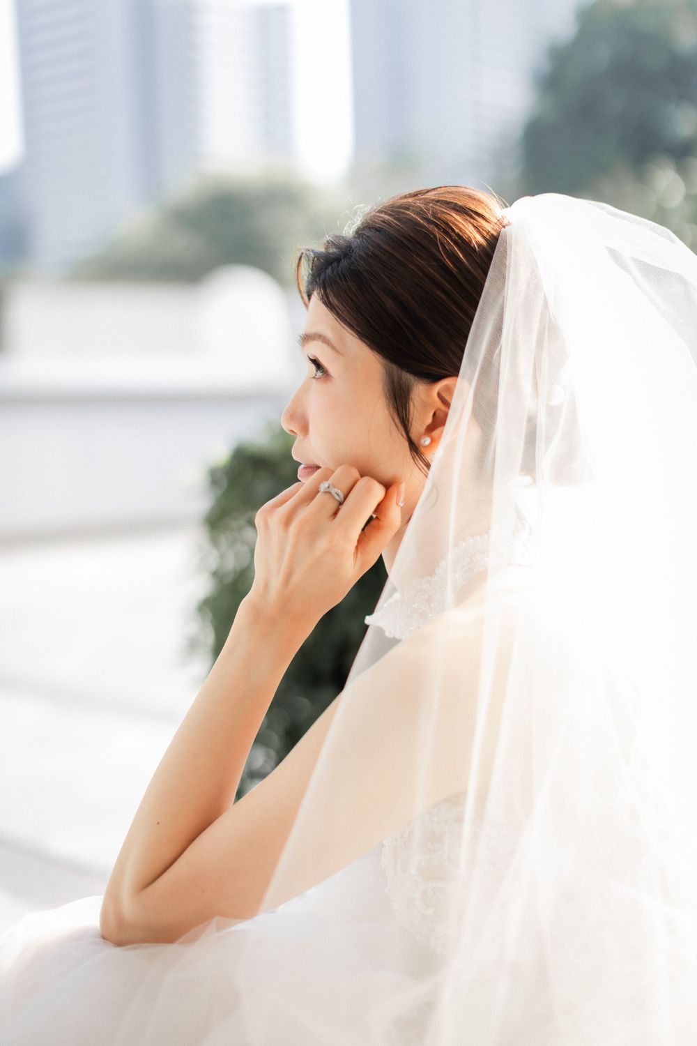Beautiful bride in white wedding dress and veil gazing sideways with city skyline background.