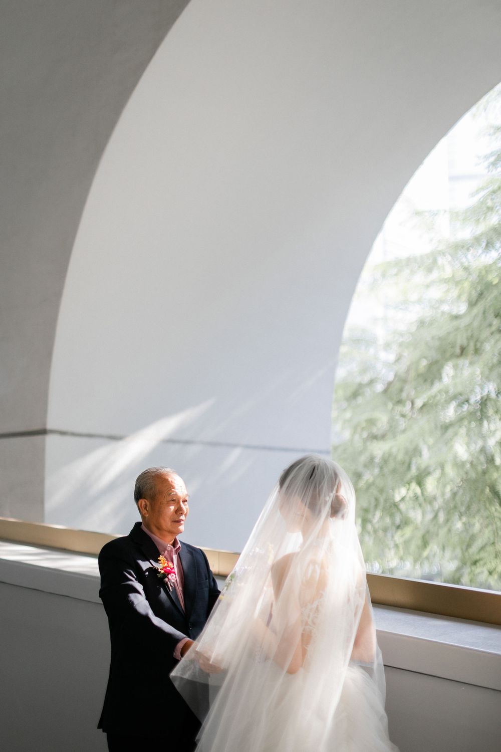 Father and bride in white gown sharing emotional pre-ceremony moment under elegant white arch.