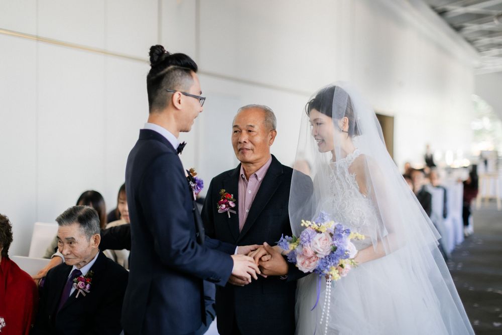 Father giving away bride in white gown and veil to groom during wedding ceremony.