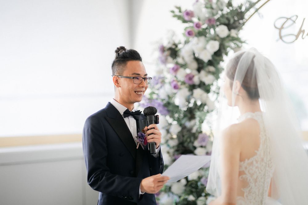 Groom reading heartfelt vows from paper to bride at floral arch wedding altar.