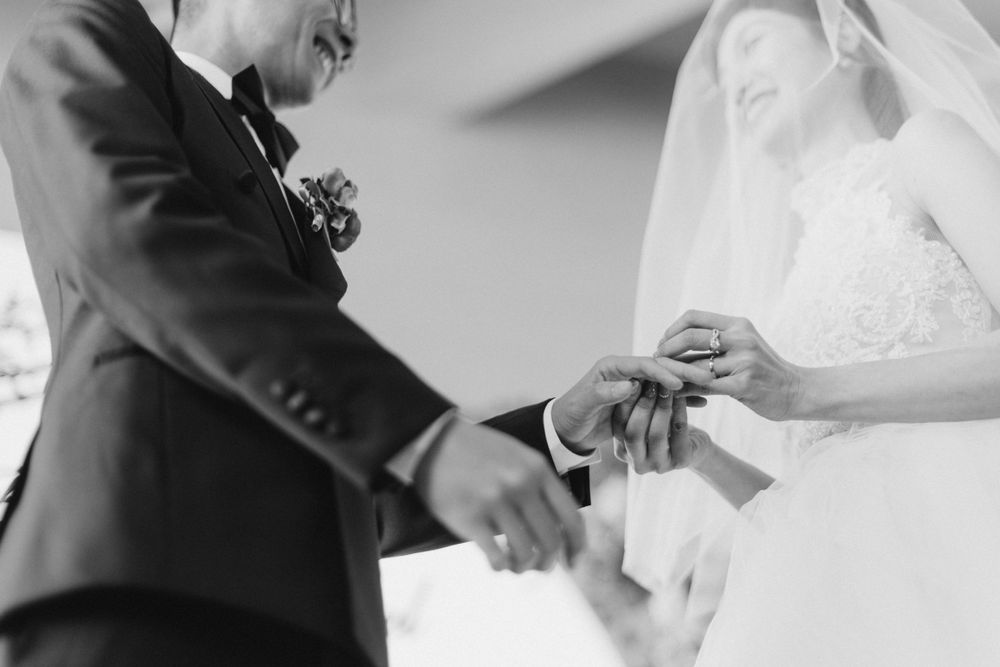 Groom places wedding ring on brides finger during emotional black and white ceremony moment.