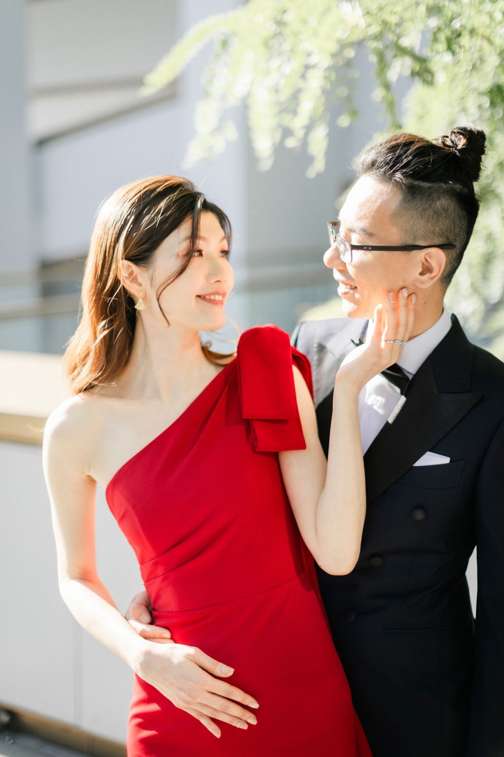Couple shares tender moment outdoors, bride in red dress and groom in black tuxedo.