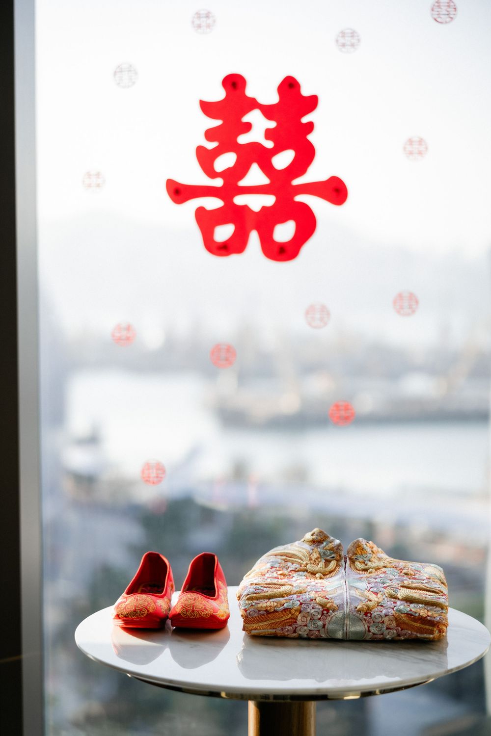 Chinese double happiness symbol with red bridal shoes and traditional kua on table by window.