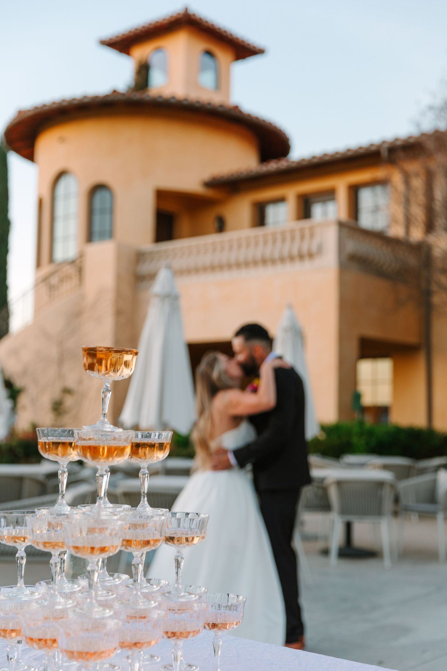 A champagne tower display with glasses at an elegant outdoor wedding venue with Mediterranean architecture.