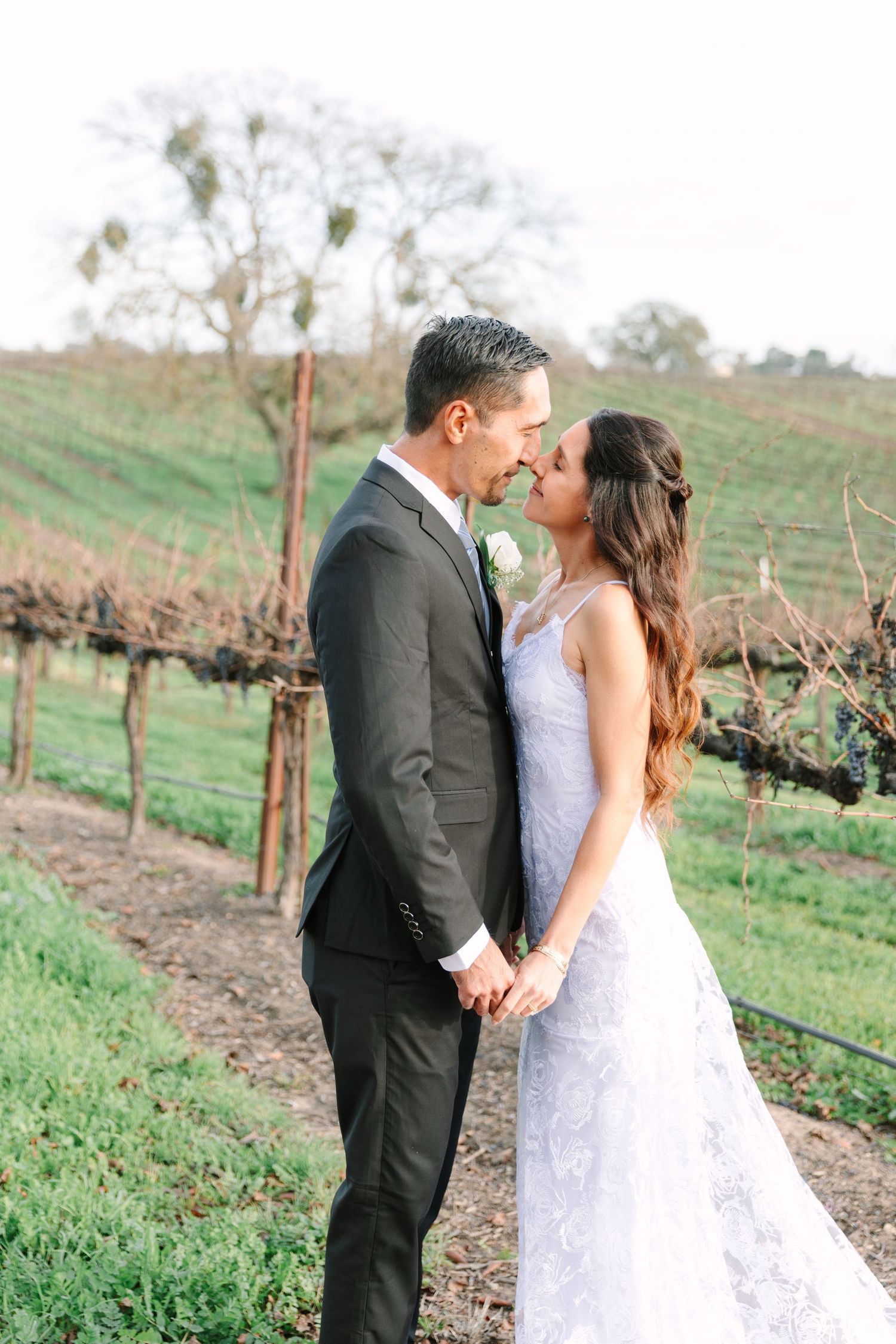 A romantic wedding couple sharing an intimate moment among vineyard rows at sunset.