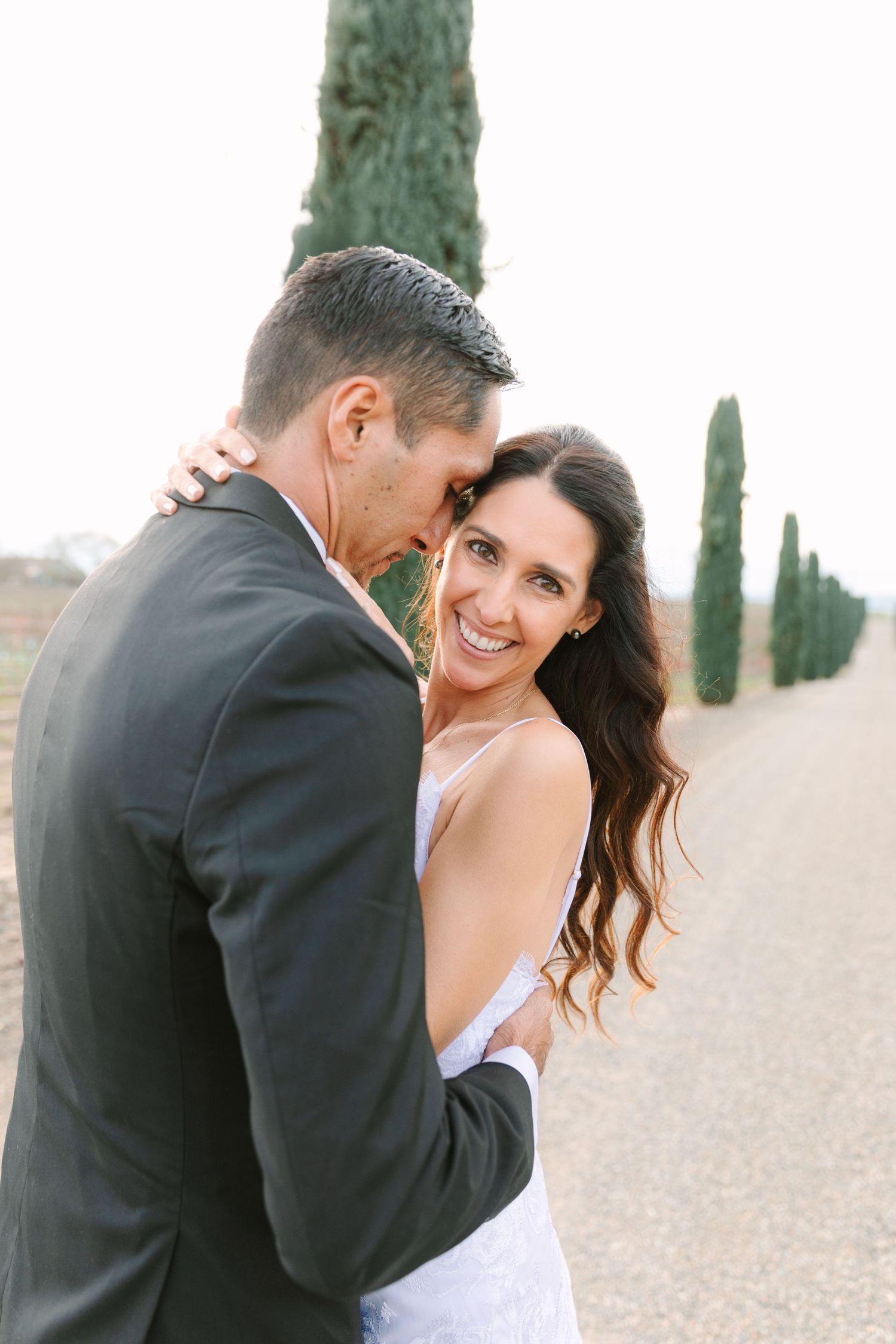 A tender moment between newlyweds on a cypress-lined path during their wedding photoshoot.