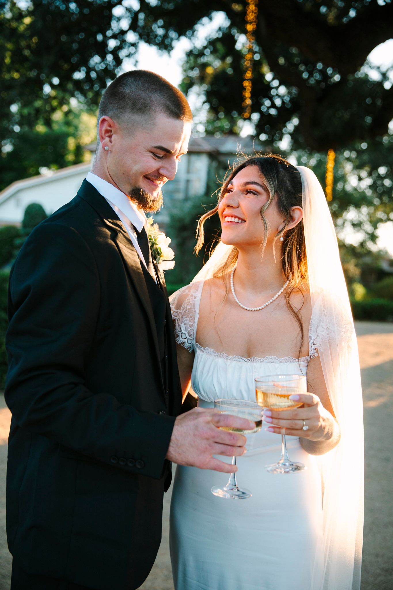 Newlyweds share a joyful moment outdoors with champagne glasses at sunset during their wedding celebration.