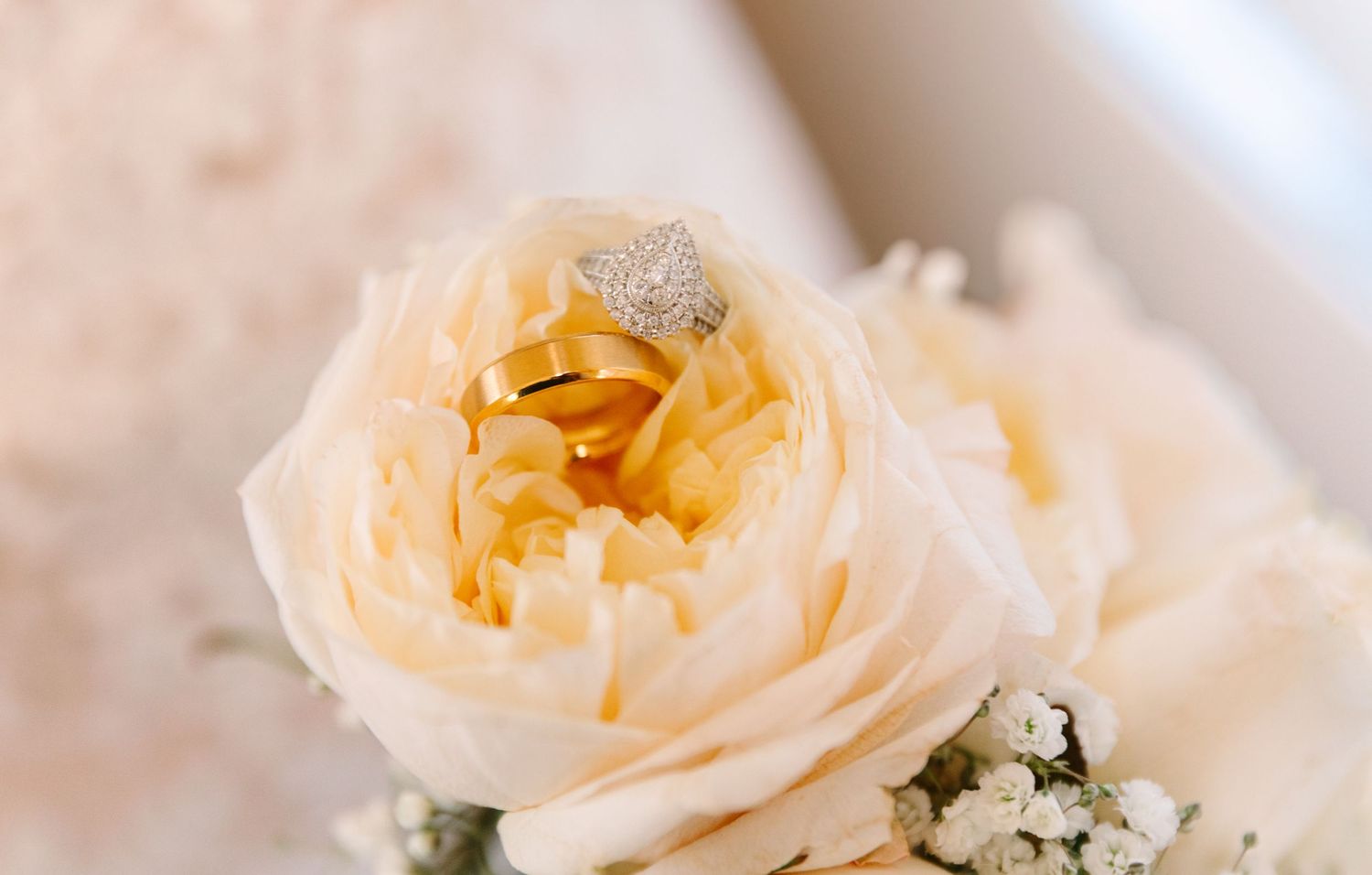 Delicate peach garden rose blooms displaying wedding rings arranged with white baby's breath flowers create a romantic floral composition.