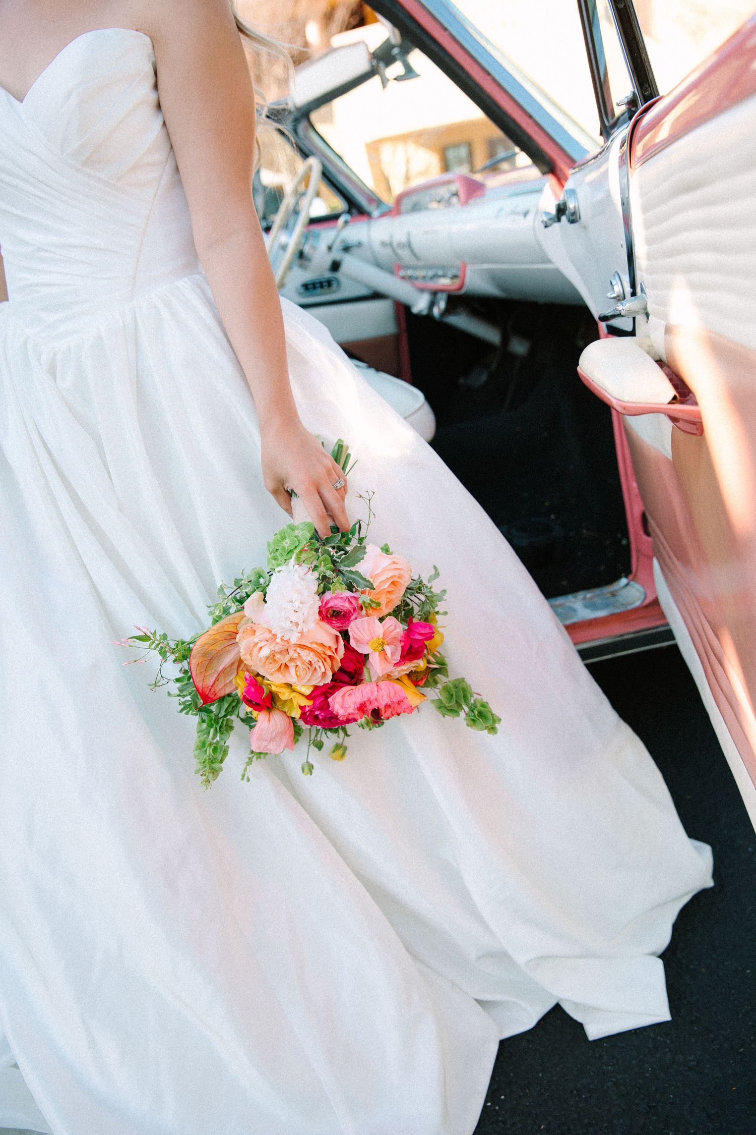 Wedding dress detail with vibrant coral and pink floral bouquet against white fabric.