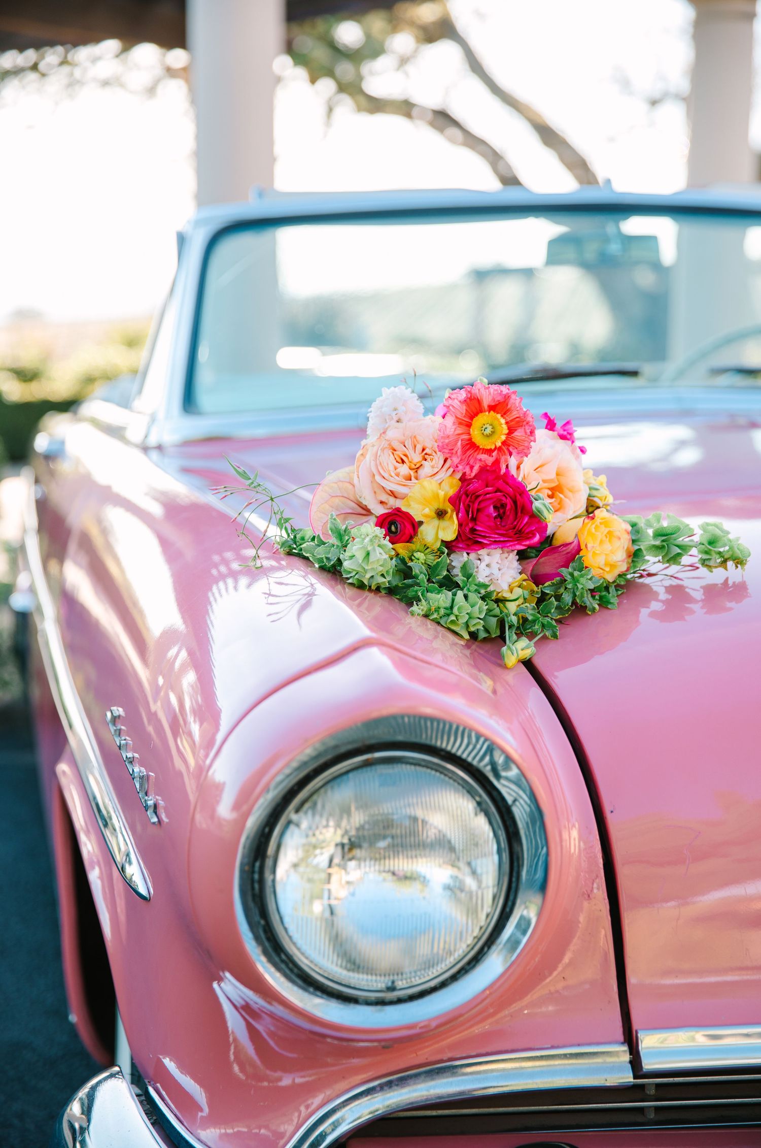 A vintage pink car decorated with colorful flowers and roses on its hood.