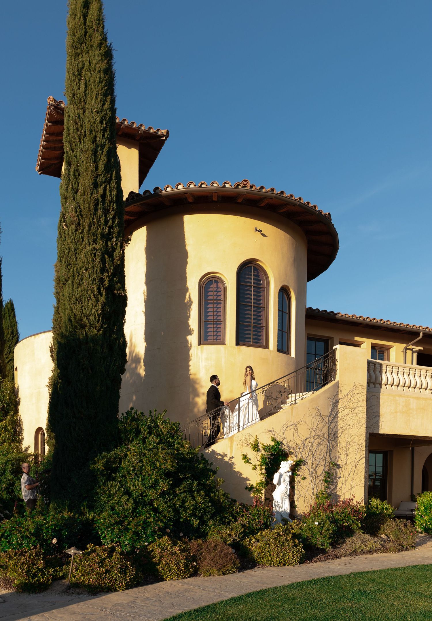Mediterranean style villa with curved turret and cypress trees against blue sky in panoramic view sequence.