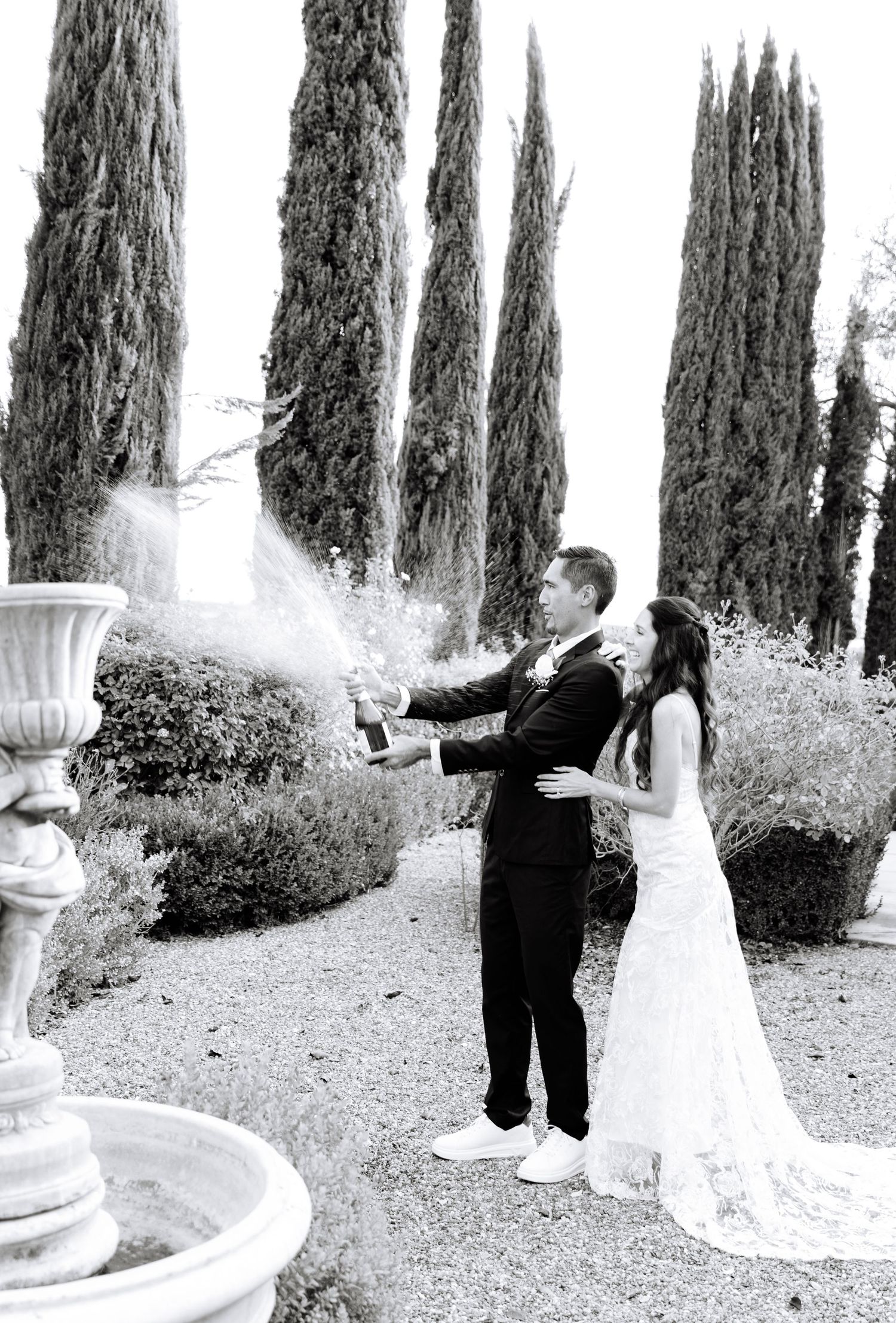 Black and white panoramic wedding photo series showing couple posing among tall cypress trees and garden urns.