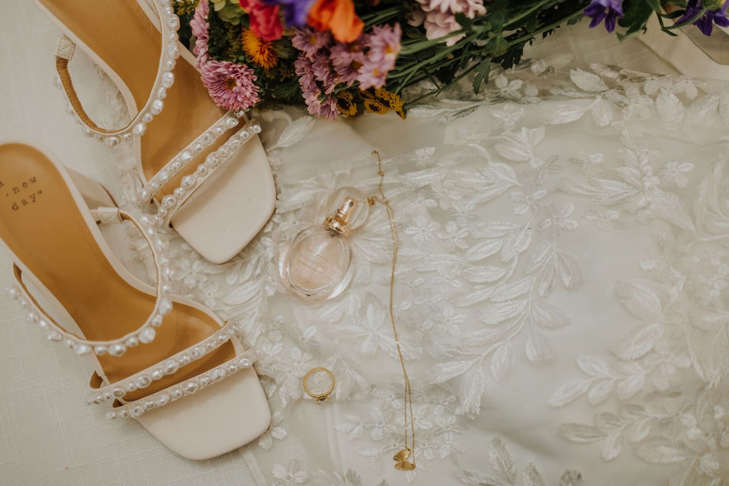 Wedding details featuring delicate floral arrangements and bridal accessories on white lace.